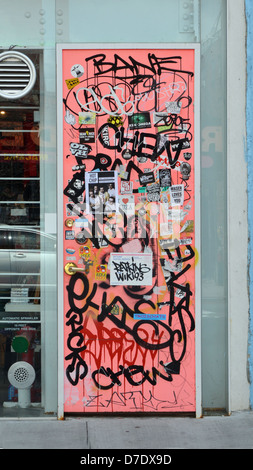 Graffiti, Aufkleber und Tags an der Tür zum Bekleidungsgeschäft Grippo Art + Design in der Grand Street in Williamsburg, Brooklyn, New York Stockfoto