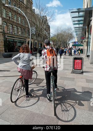 Ein Paar auf Fahrrädern, die sich entlang der Fußgängerzone mit ihren Geschäften schauten Straße in Cardiff City Centre St Davids 2 Bezirk in Spring Wales UK KATHY DEWITT Stockfoto