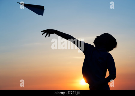 Junge werfen ein Papier Flugzeug bei Sonnenuntergang. Silhouette Stockfoto