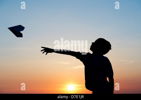 Junge werfen ein Papier Flugzeug bei Sonnenuntergang. Silhouette Stockfoto