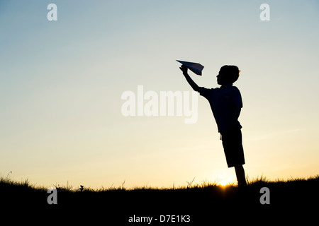 Junge werfen ein Papier Flugzeug bei Sonnenuntergang. Silhouette Stockfoto