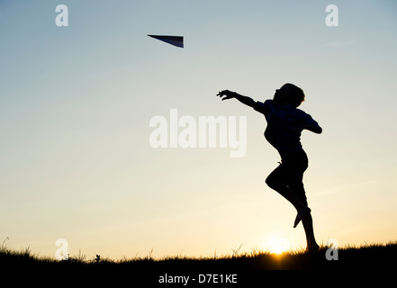 Junge werfen ein Papier Flugzeug bei Sonnenuntergang. Silhouette Stockfoto