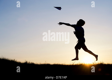 Junge werfen ein Papier Flugzeug bei Sonnenuntergang. Silhouette Stockfoto