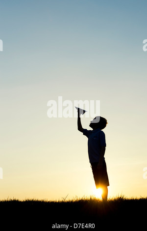 Junge werfen ein Papier Flugzeug bei Sonnenuntergang. Silhouette Stockfoto