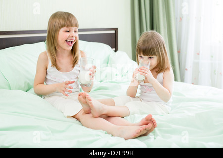 Zwei kleine Mädchen Konsummilch aus Gläsern auf Bett Stockfoto