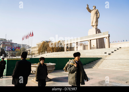 Uyghar Männer gehen durch die riesige Statue von Mao Zedong in Kashgar, Xinjiang, China Stockfoto
