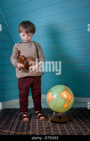 Kleiner Junge betrachtet man eine aus Holz geschnitzten Elefanten in seinen Händen stehen neben einem beleuchteten Globus zeigt Afrika und Südamerika Stockfoto