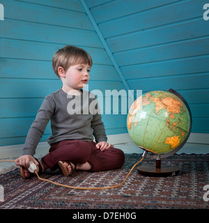 Ein junges Kind schaut eine beleuchtete Kugel denken weit Weg stellen sitzen in einem gemütlichen Dachgeschoss Raum zu Hause Licht Stockfoto