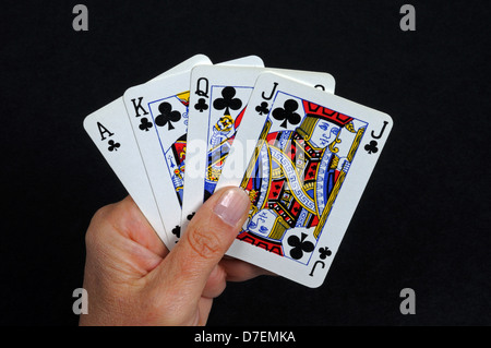 Hand mit Spielkarten, Ass, König, Dame und Jack der Vereine vor einem schwarzen Hintergrund. Stockfoto