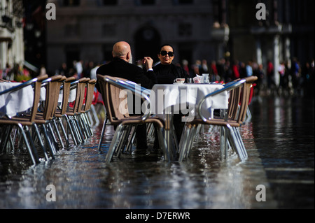 Ein paar frühstücken auf der Terrasse vom "Acqua Alta" am Markusplatz, Venedig überflutet. Stockfoto