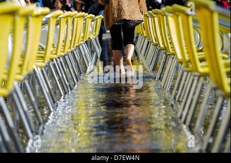 Ein Touristen-Spaziergang im Wasser um Stühle und Tische von einem der Cafés am Markusplatz, Venedig, Italien. Stockfoto