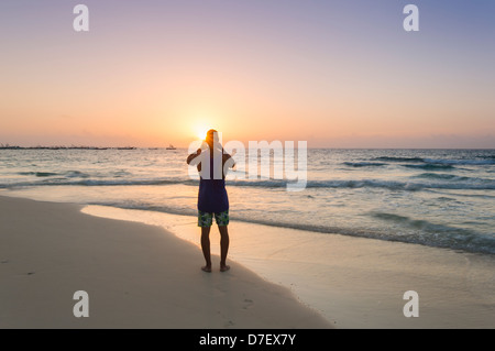 Mann, der an einem Strand in Silhouette Fotografieren bei Sonnenaufgang Stockfoto