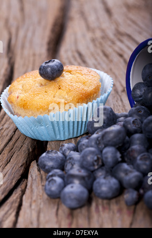 Ein Blaubeer-Muffin und eine alte Emaille-Tasse gefüllt mit Heidelbeeren auf alten Holztisch Stockfoto