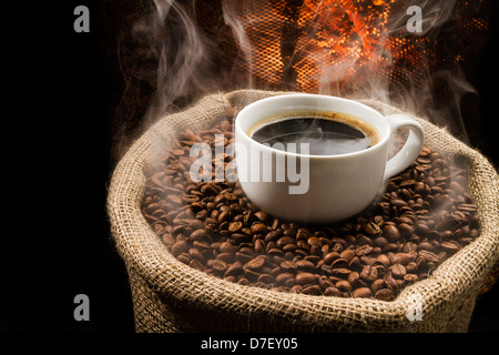 Sack voller noch warm, frisch gerösteten Kaffeebohnen mit dem Becher in der Mitte. Stockfoto