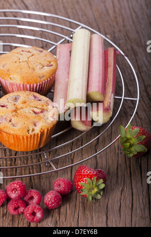 Zwei ganze Erdbeer Rhabarber und Himbeer Muffins mit frischem Obst auf einem Kuchengitter Kuchen Stockfoto