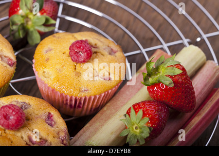 Einige Erdbeer-Rhabarber und Himbeer-Muffins und frisches Obst auf einem Kuchen Draht rack Stockfoto