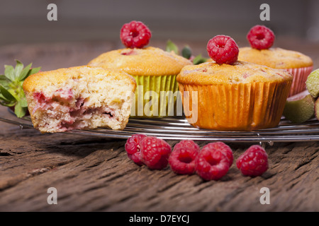 Einige ganze Muffins und eine angebissene Muffin auf einem Kuchengitter Kuchen mit frischen Himbeeren auf der Vorderseite Stockfoto