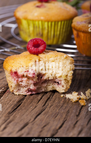 Einige ganze Muffins auf einem Kuchengitter Kuchen im Hintergrund und einem gebissen Muffin in der front Stockfoto