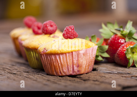 Vier ganz lecker Obst-Muffins mit einer Himbeere oben in einer Reihe auf einem alten Holzbrett Stockfoto
