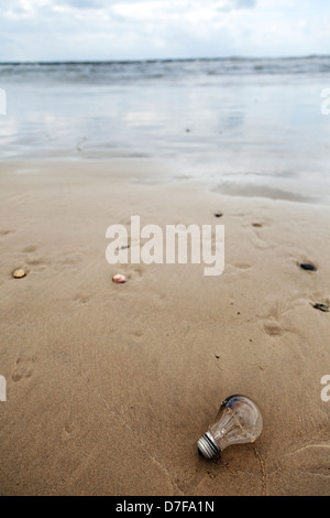 Eine gebrauchte ausgebrannte Glühbirne aufgegeben am Sandstrand bei schlechtem Wetter. Bezieht sich auf Energieeinsparung Stockfoto