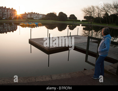 Dame, die gerade am frühen Morgen Sonnenaufgang durch einen See mit Booten Stockfoto