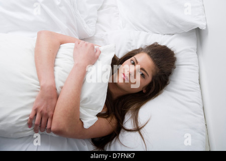 Eine traurig aussehende junge Frau im Bett umarmt eine Kissen liegend. Stockfoto