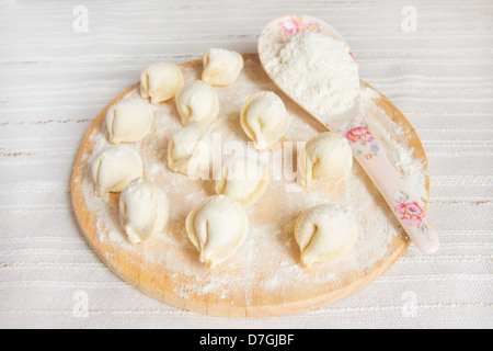 Ungekochten Knödel (russische traditionelle Küche - Pelmeni) auf hölzernen Druckstoffen Brett mit Mehl über Leinen Hintergrund. Stockfoto