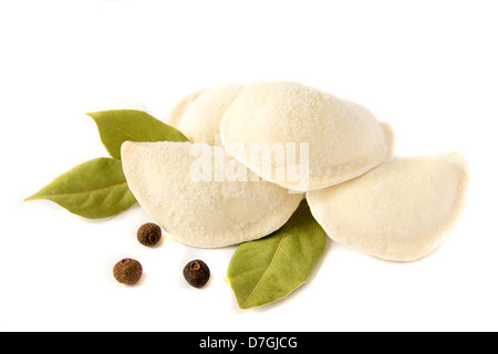 Ungekocht gefrorene Knödel (russische traditionelle Küche - Pelmeni) mit Pfeffer und Lorbeerblatt isoliert auf weißem Hintergrund hautnah. Stockfoto