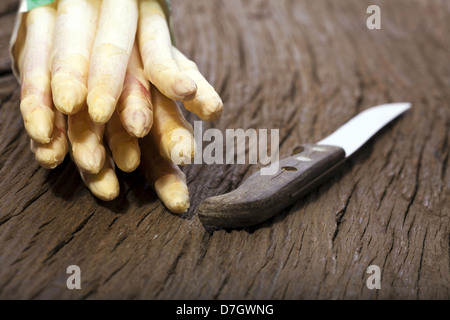 Weißer Spargel wird mit den Spitzen nach vorn auf einem Holzbrett neben einem alten Messer mit Holzgriff Stockfoto