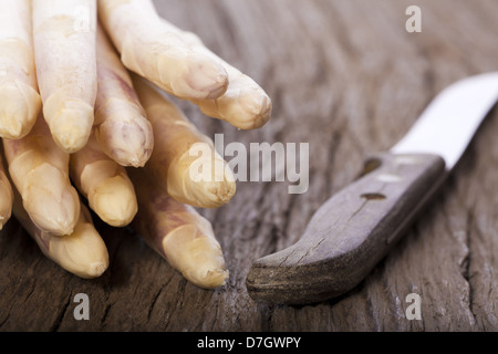 Weißer Spargel wird mit den Spitzen nach vorn auf einem Holzbrett neben einem alten Messer mit Holzgriff Stockfoto