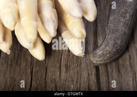 Weißer Spargel wird mit den Spitzen nach vorn auf einem Holzbrett neben einem alten Messer mit Holzgriff Stockfoto