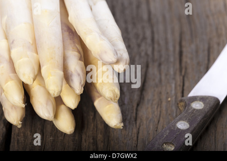 Weißer Spargel wird mit den Spitzen nach vorn auf einem Holzbrett neben einem alten Messer mit Holzgriff Stockfoto