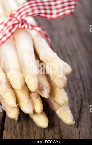 Frischer weißer Spargel mit rot-weiß karierten Webband mit den Spitzen nach vorn auf einem rustikalen Holzbrett ist gebunden Stockfoto