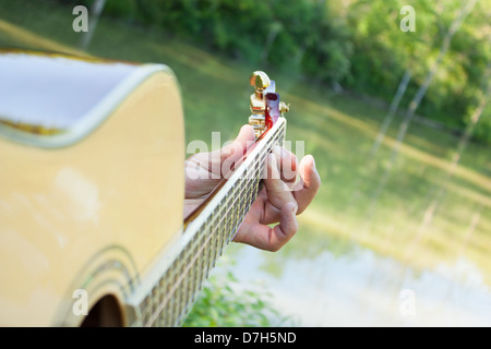 akustische Gitarre gespielt wird. Blick entlang des Halses am Teich. Stockfoto