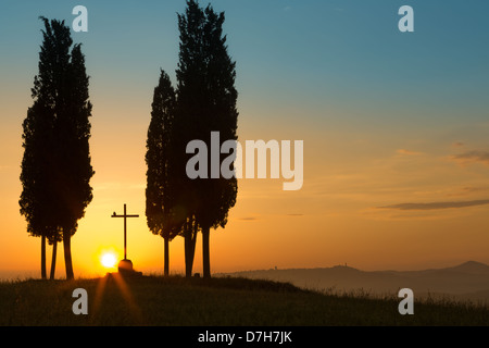 Sonnenaufgang hinter ein einsames Kreuz zwischen Zypressen liegt auf den Hügeln der Toskana in der Nähe von Pienza Italien Stockfoto