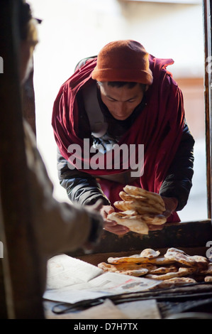 Eine buddhistische Mann Bögen als er kauft seinen Morgen Brot aus dem Tandoor Ofen. Stockfoto