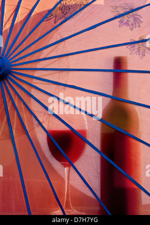 ROTWEIN-GLASFLASCHE IM FREIEN URLAUB EXOTISCHER CHINESISCHER Sonnenschirm im Garten mit Rotweinglas und Flasche in diffuser Silhouette dahinter Stockfoto