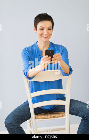 Frau auf Stuhl sitzend und mit Handy Stockfoto