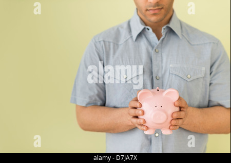 Junger Mann verwahrenden Piggy bank Stockfoto