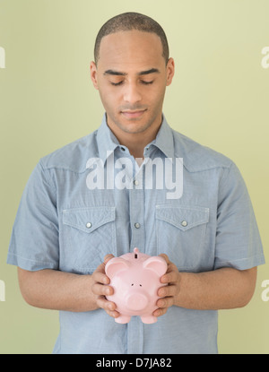 Junger Mann verwahrenden Piggy bank Stockfoto