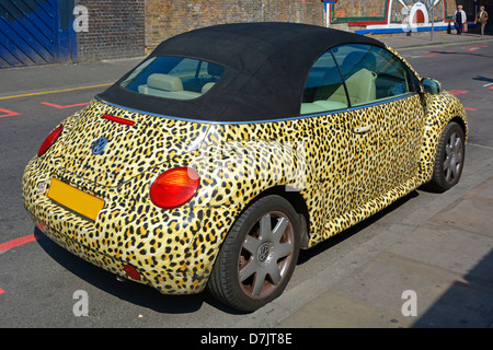 Das Leopardenfell-Muster bedeckt die Karosserie des VW Beetle Car mit schwarzem Vinyldach, das im sonnigen Brick Lane Tower Hamlets East London England UK geparkt ist Stockfoto