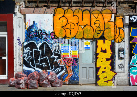 Ladenfront mit Brettern vernagelt und bedeckt in Graffiti Grafitti mit Müllsäcke und Bauunternehmen vor Ort Sicherheitshinweis Stockfoto