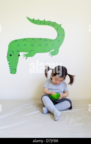Korean American Girl Essen vom grünen Schale mit grünen Krokodil Wandkunst hinter Stockfoto