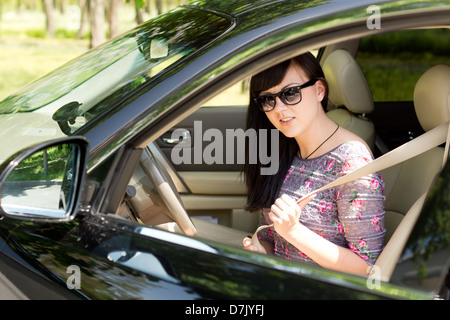 Nahaufnahme von eine attraktive Brünette Frau auf ihren Sicherheitsgurt im Auto sitzen. Stockfoto