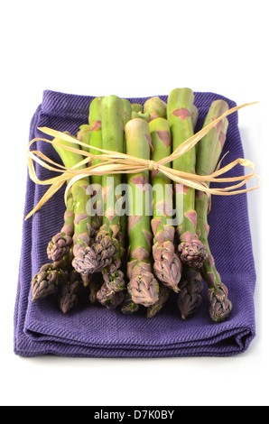 Frischen rohen Spargel Haufen auf lila Serviette auf weißem Hintergrund in Hochformat Stockfoto