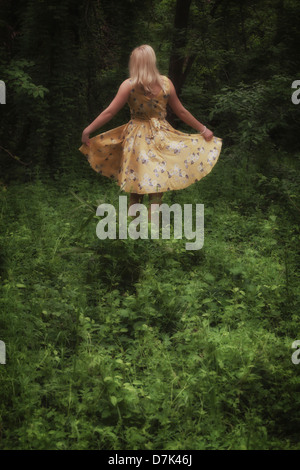 eine blonde Mädchen mit einem gelben Kleid tanzt im Wald Stockfoto