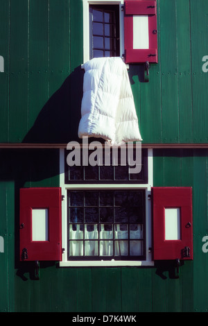 eine weiße Decke aus einem Fenster von einem grünen Holzhaus mit roten Fensterläden hängen Stockfoto