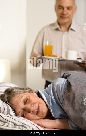 Liebevoller senior Ehemann Frühstück, schlafende Frau Stockfoto