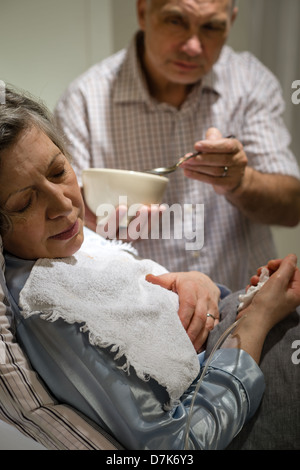 Reifer Mann hilft seiner kranken Frau Fütterung Suppe Stockfoto