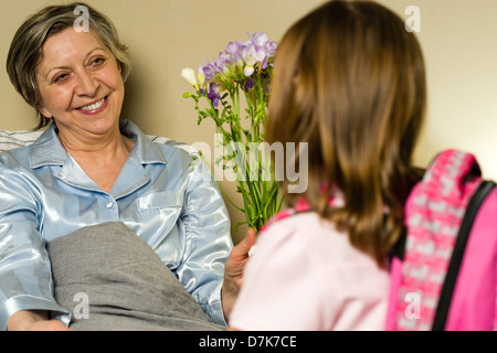 Kleines Mädchen besuchen kranke Großmutter Blumen schenken Stockfoto
